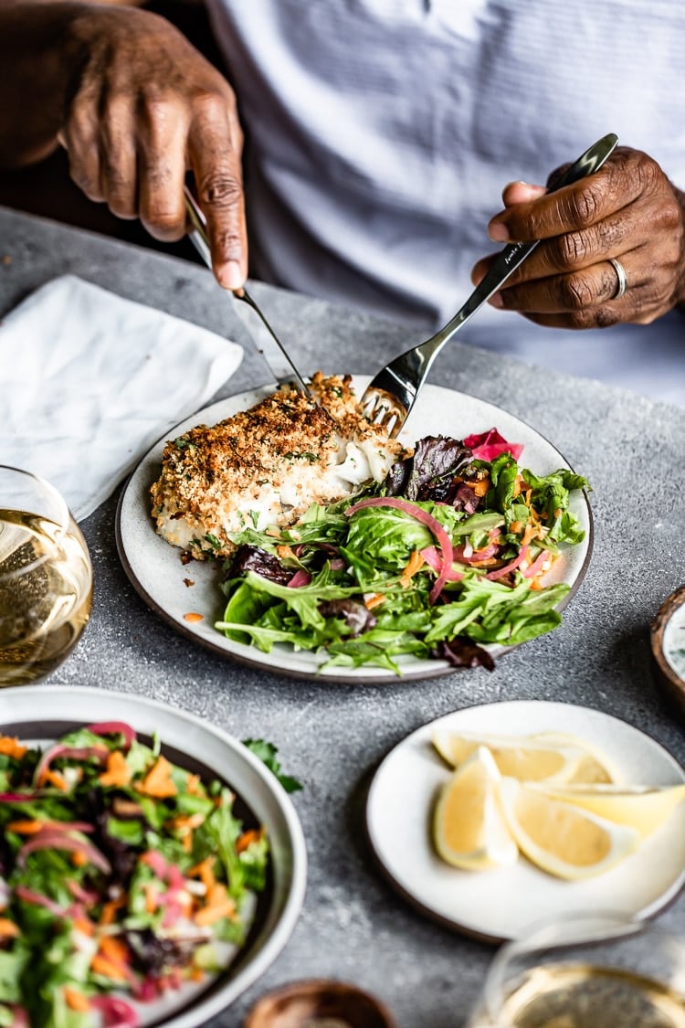 Man eating baked breaded cod with a salad on the side