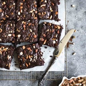 Spelt flour almond butter brownies cut into squares and served on a wire rack with a knife on the side.