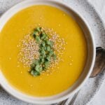 A bowl of Roasted Kabocha Squash Soup with Sesame Seeds with a spoon on the side
