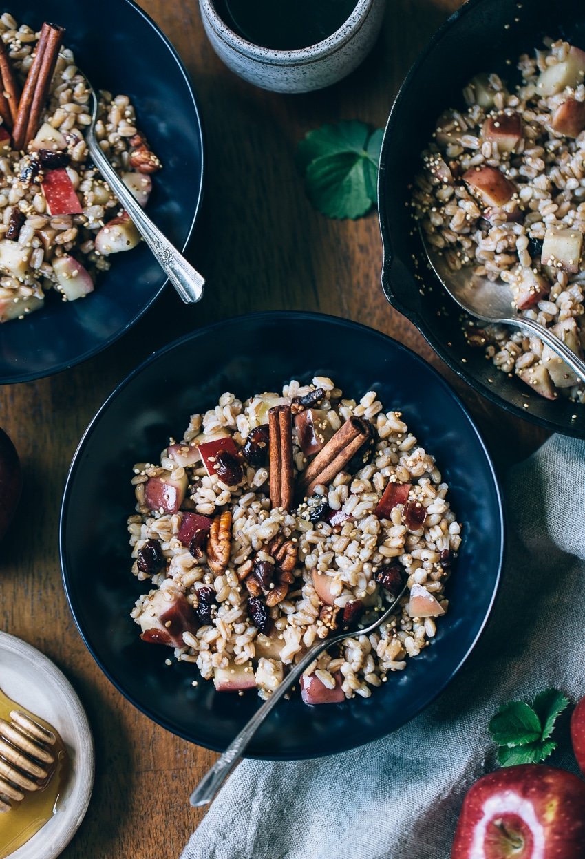 several bowls of farro breakfast bowl topped of with apples and cinnamon stick