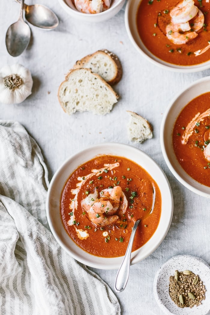 Three bowls of Tomato Curry Soup with Cumin Roasted Shrimp are photographed from the top with sliced bread, garlic, and shrimp