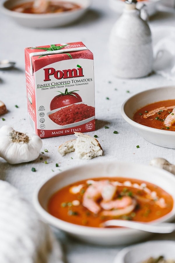 A big bowl of Gluten Free Tomato Soup Recipe with Cumin Roasted Shrimp is photographed along with a box of Pomi chopped tomatoes 
