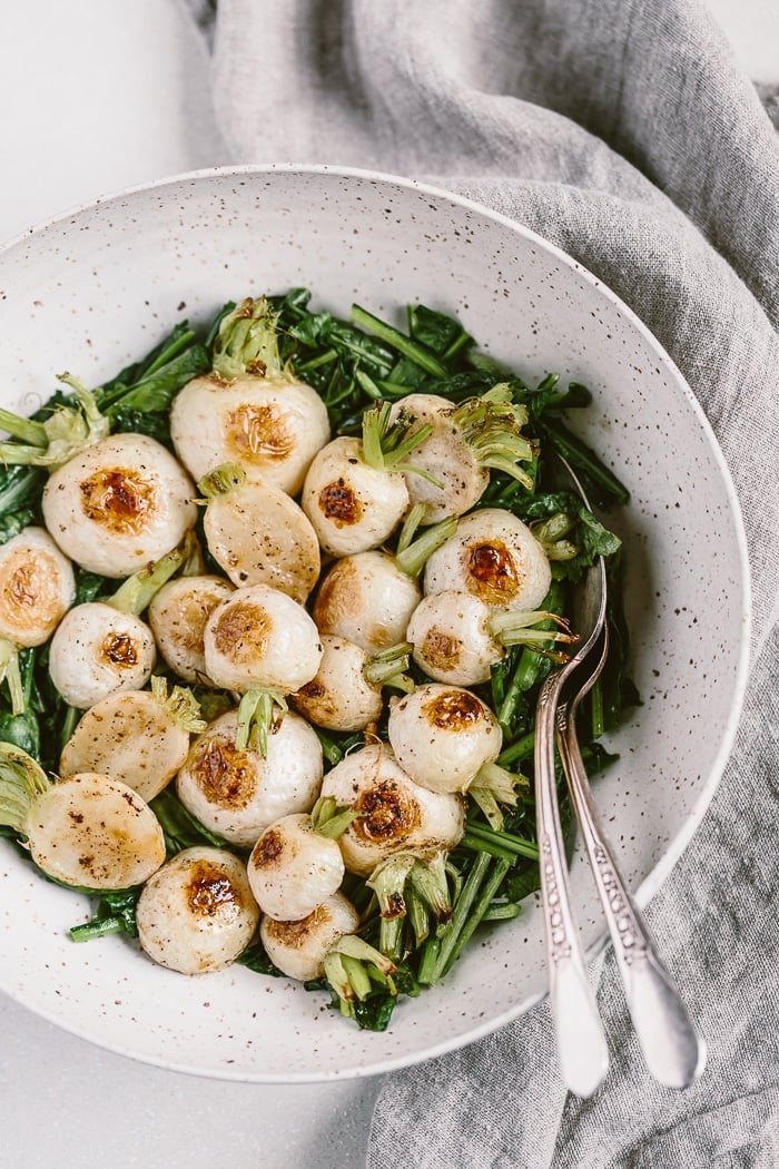 Roasted Japanese Turnips served in a bowl over sautéed leaves.