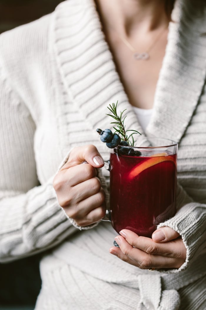 A woman holding a glass of honey sweetened blueberry hot toddy