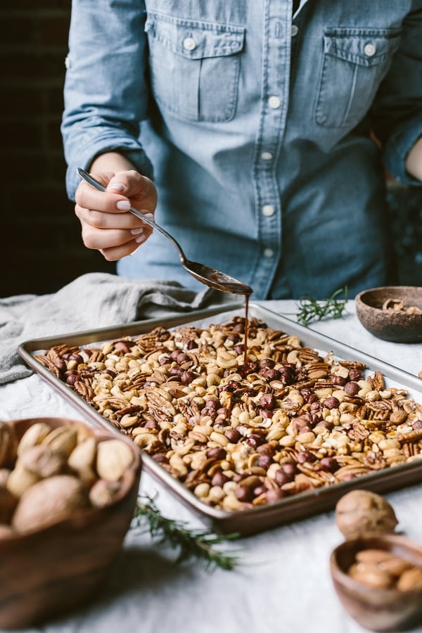 Sweetener being drizzled over Spicy Candied Nuts on a sheet pan
