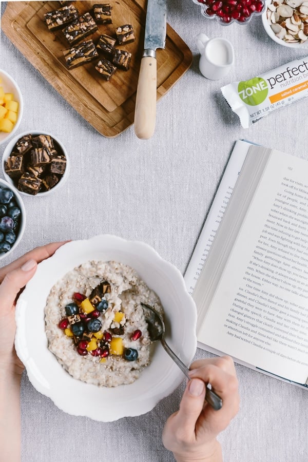 A woman is photographed from the top view as she is eating oatmeal while reading a book.