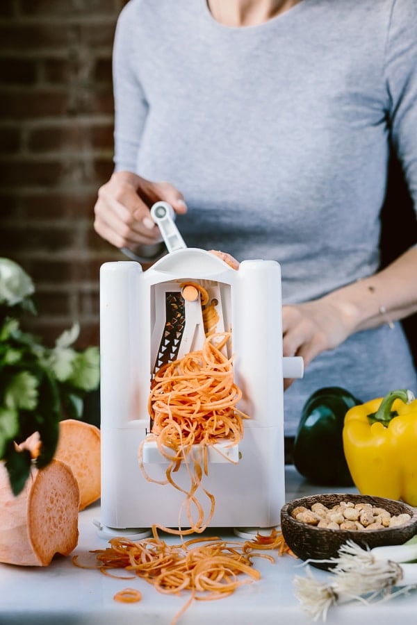 A woman is photographed as she is spiralizing sweet potato noodles
