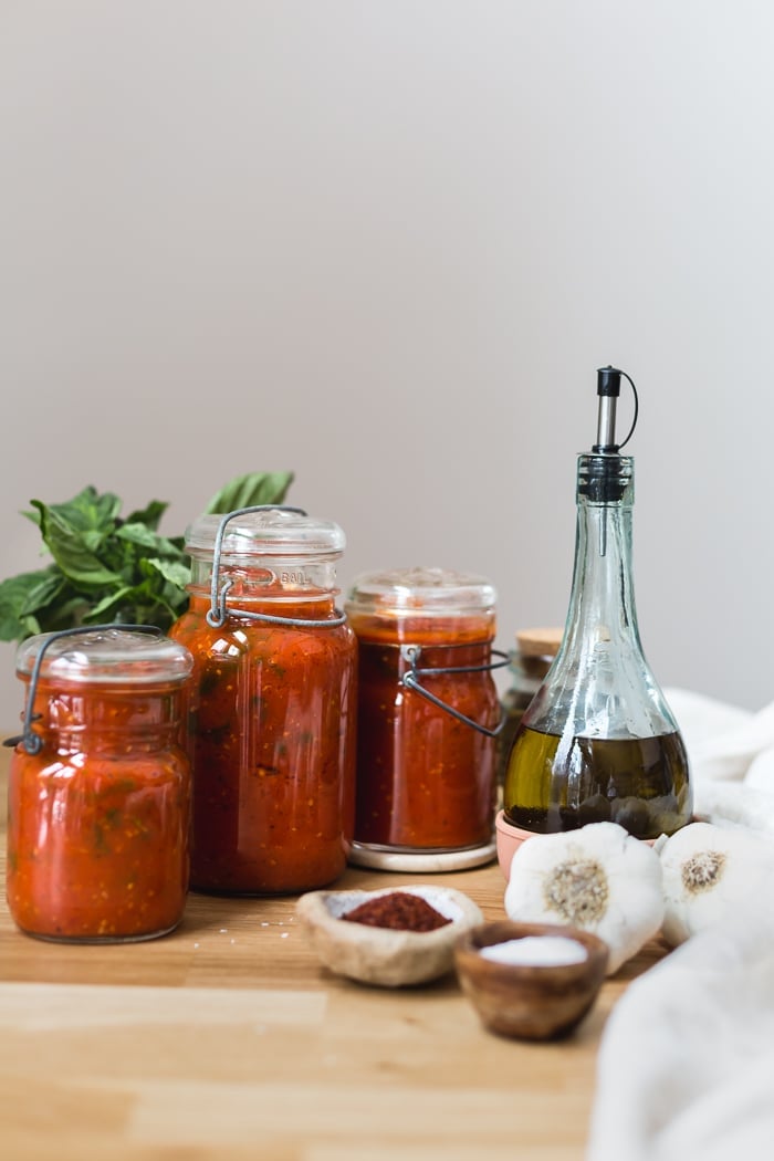 Homemade Tomato Sauce placed in jars with olive oil and garlic on the side