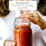 A woman is holding a jar of Homemade Tomato Basil Sauce in her hands