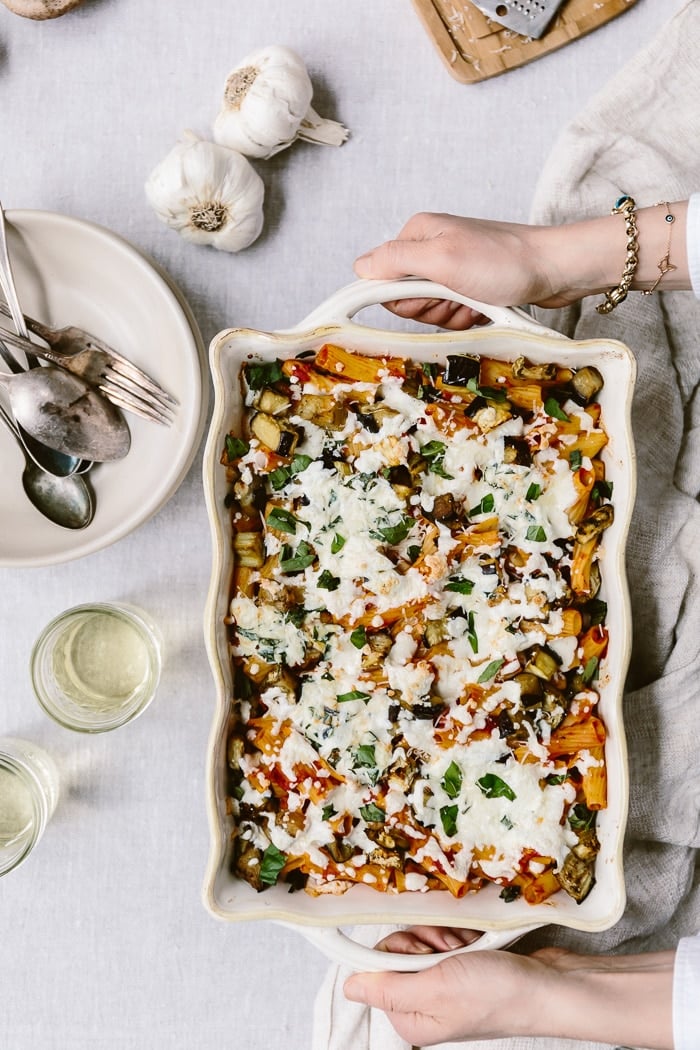 a woman is serving baked ziti with eggplant and ricotta