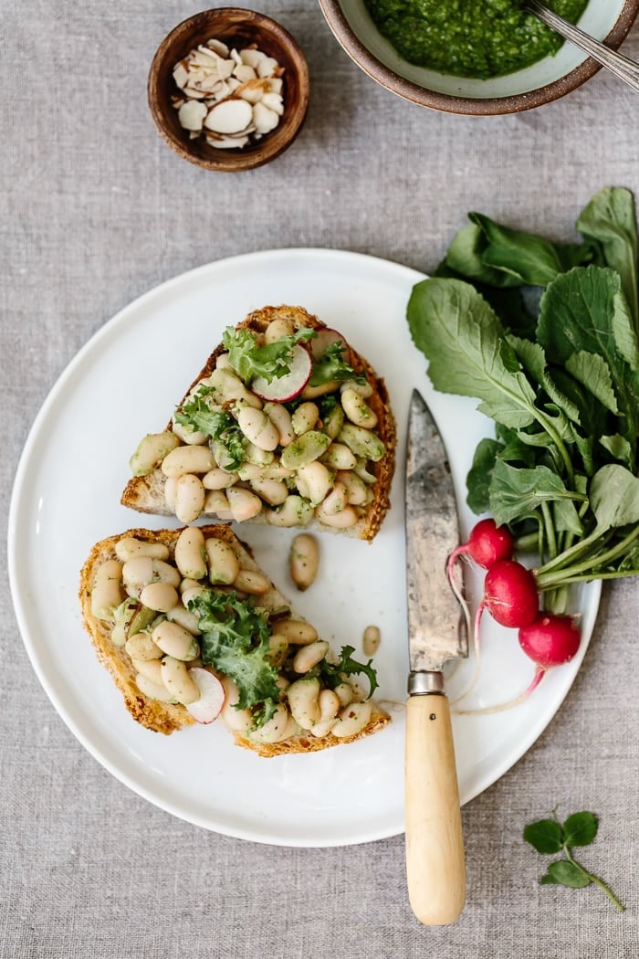 A toast spread with arugula White Bean Salad and small radishes on the side