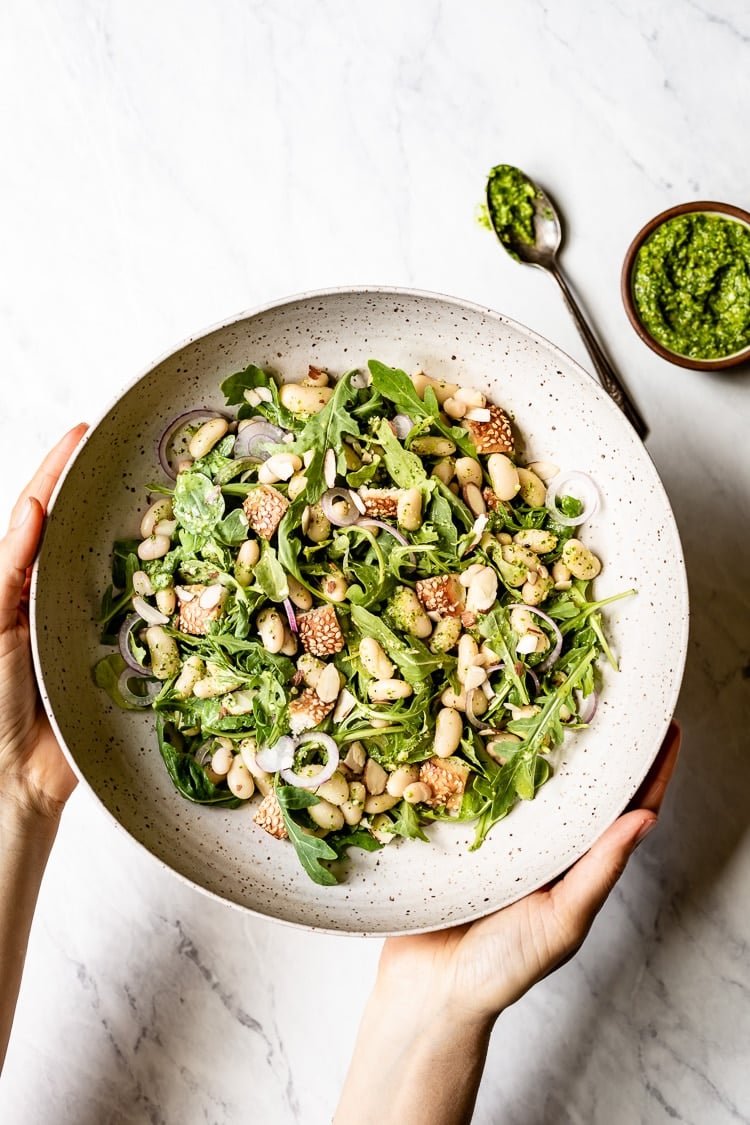 Warm White Bean Arugula Salad mixed in with arugula photographed from the top view as someone is holding it.