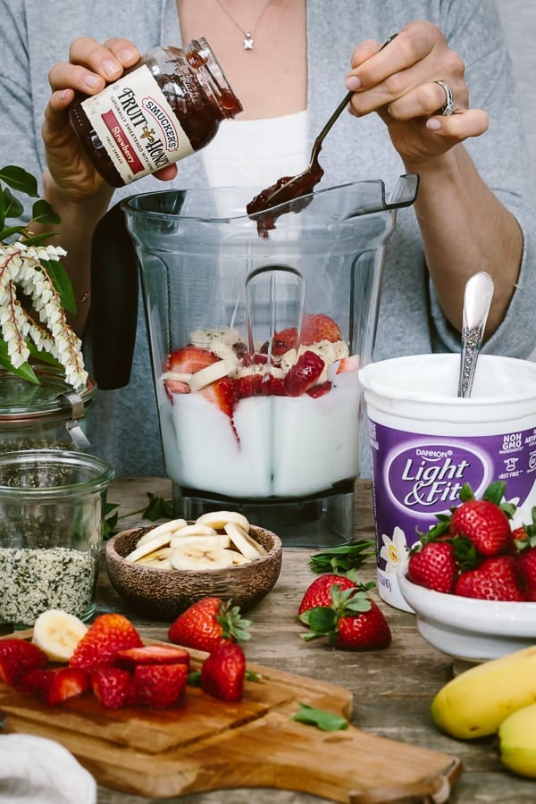 A woman is photographed from the front view as she making Strawberry Banana Yogurt Smoothie