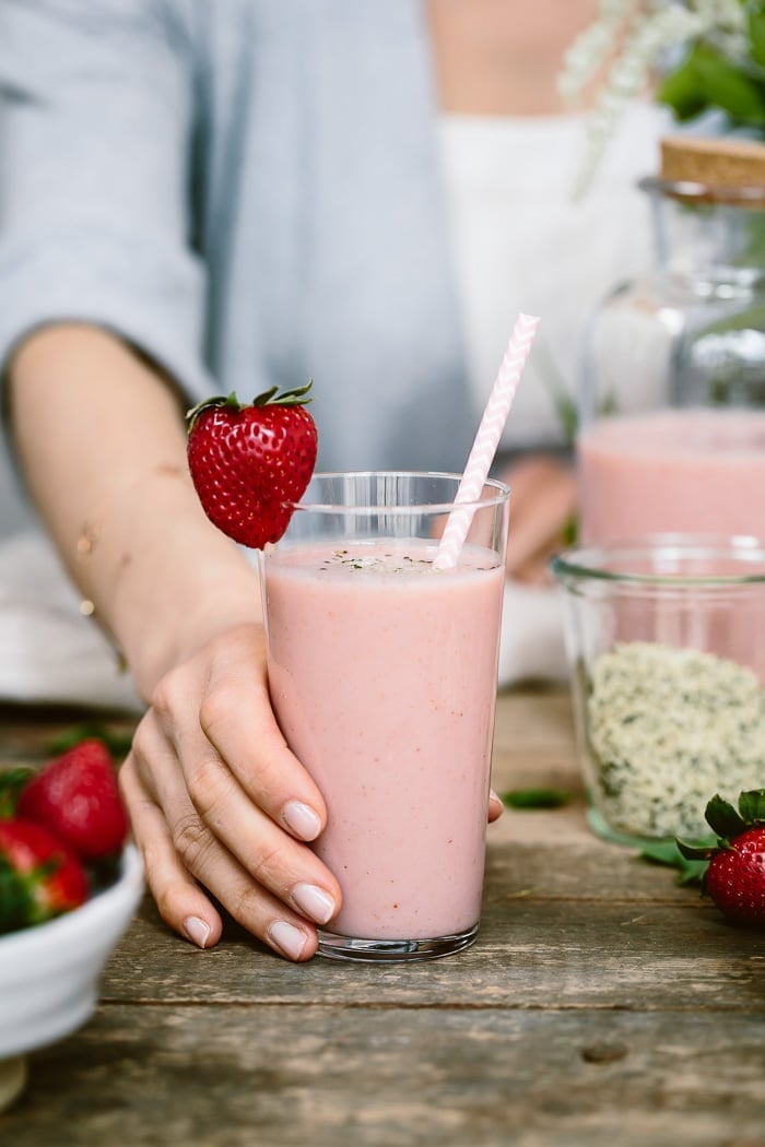 A woman is serving a glass of strawberry banana smoothie with yogurt.