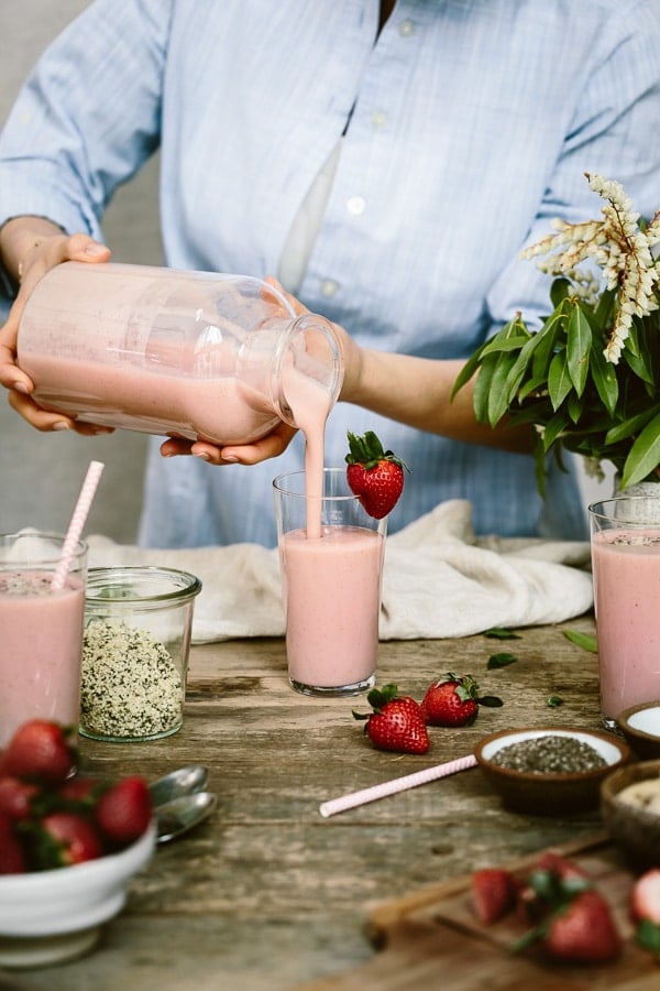 A woman is pouring Strawberry Banana Smoothie with vanilla yogurt into a glass.