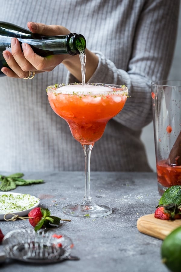 A woman is pouring champagne in a glass to make this Strawberry Champagne margarita recipe
