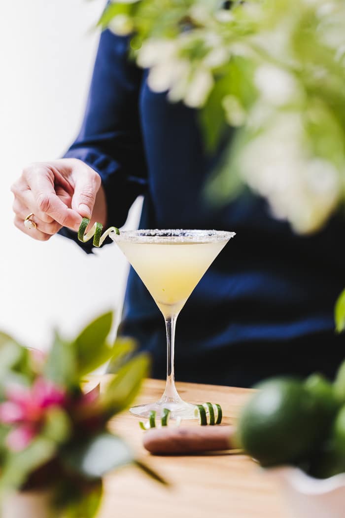 A woman is holding a lime garnish for the Recipe for Lime Drop Martini made with mint flavored simple syrup.