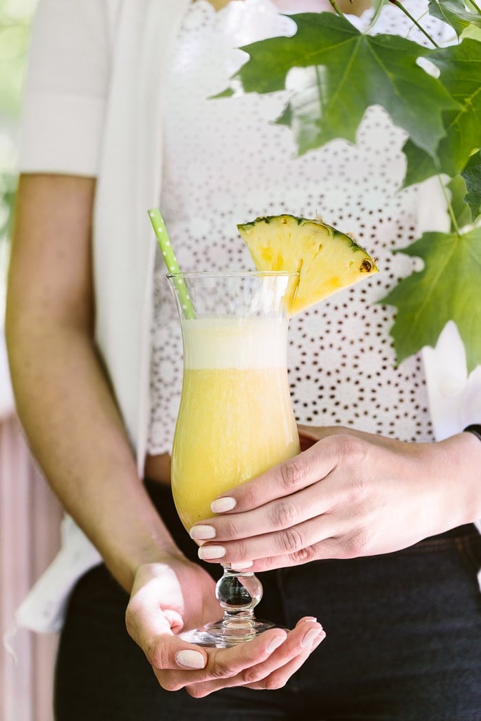 A woman is holding a glass of Pina Colada Smoothie garnished with a pinapple