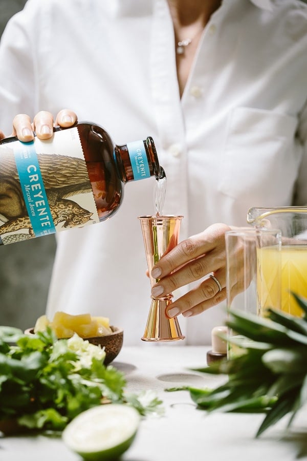 a woman is pouring mezcal in a measuring cup for drinks