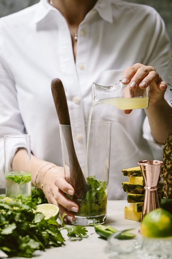 A woman is photographed as she is making a mezcal pineapple cocktail