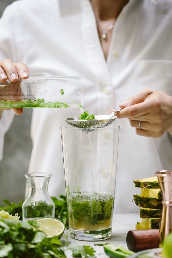 a woman is draining the chopped jalapenos from the liquid to make a mezcal cocktail