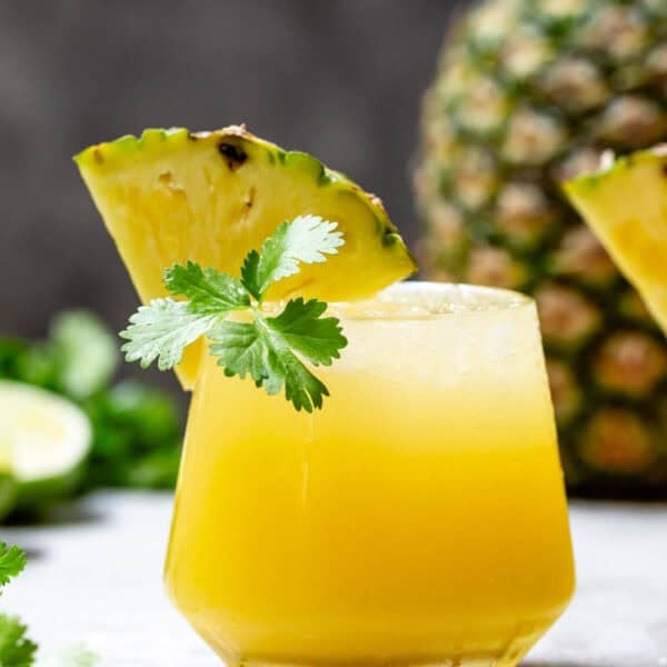 Pineapple mezcalita in a glass garnished with a pineapple wedge and fresh cilantro.