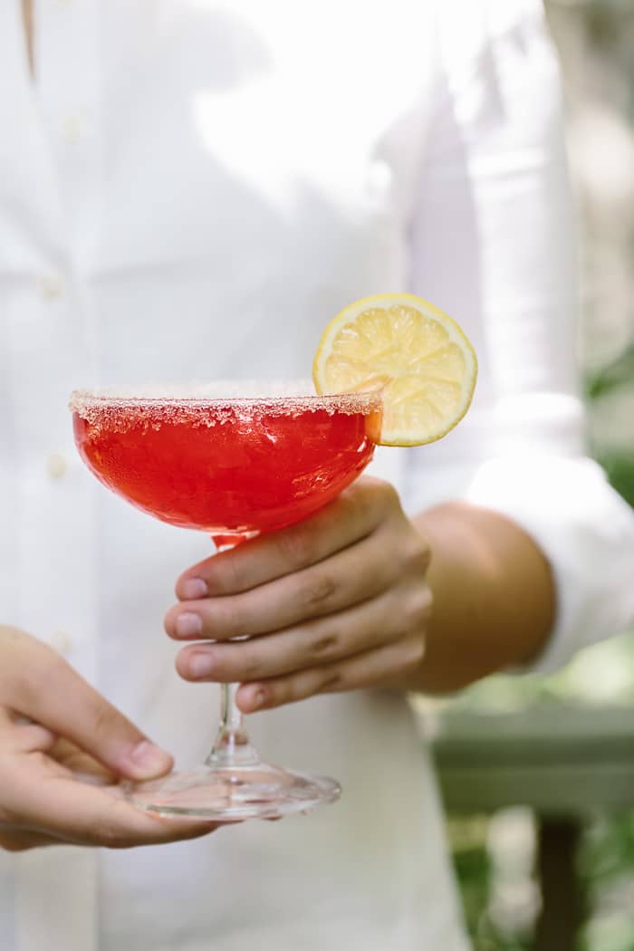 Raspberry Lemon Drop Martini with lemon garnish is photographed in the hands of a woman.