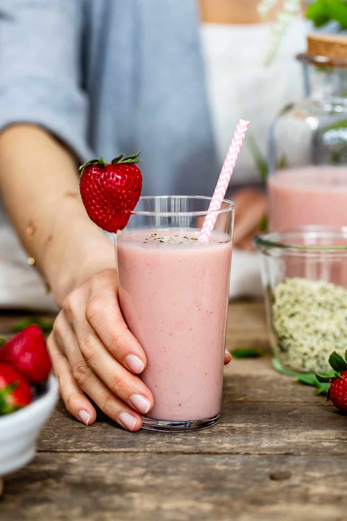 A person is serving a strawberry banana smoothie with yogurt in a glass.