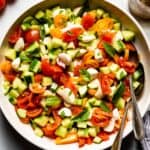 tomato cucumber mozzarella salad in a bowl with two spoons on the side