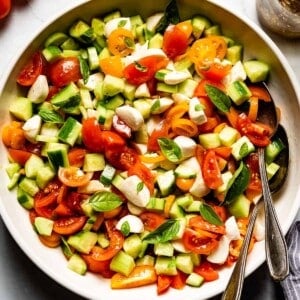 tomato cucumber mozzarella salad in a bowl with two spoons on the side