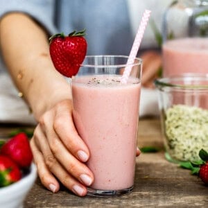 Person serving a strawberry smoothie in a glass.