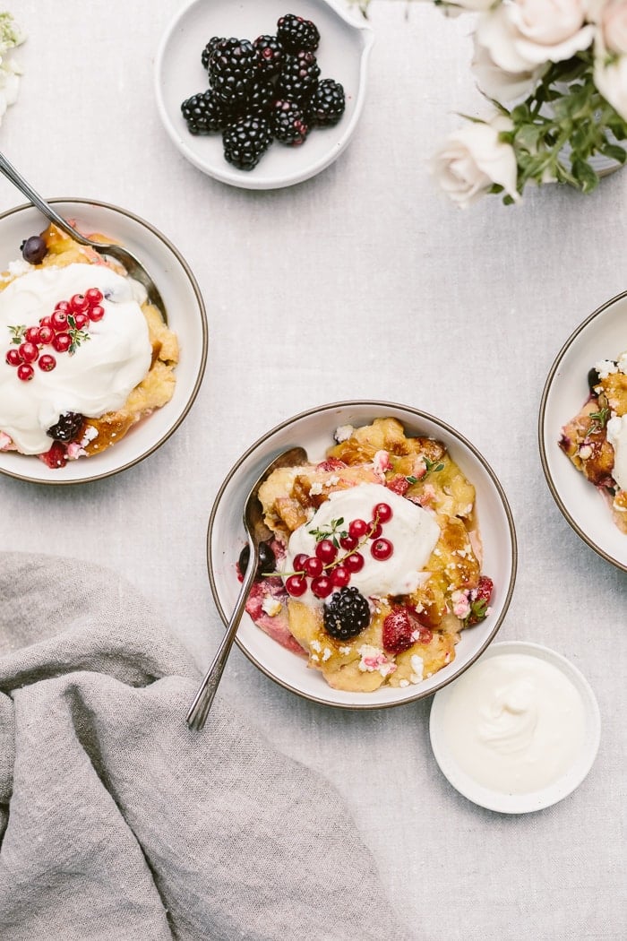 Portioned goat cheese berry bread pudding in bowls with creme fraiche on the side.