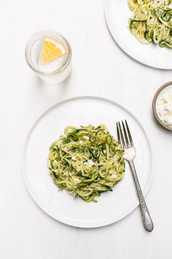 5-Ingredient Zucchini Noodles Recipe - A vegetarian spiralized zucchini noodle pasta recipe made with olive oil, garlic, dill and feta placed on a plate with a fork on the side.