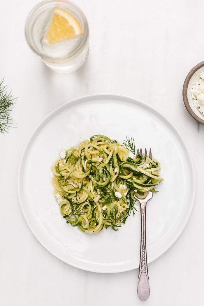 Vegetarian zucchini zoodles on a plate topped off with feta cheese and dill.