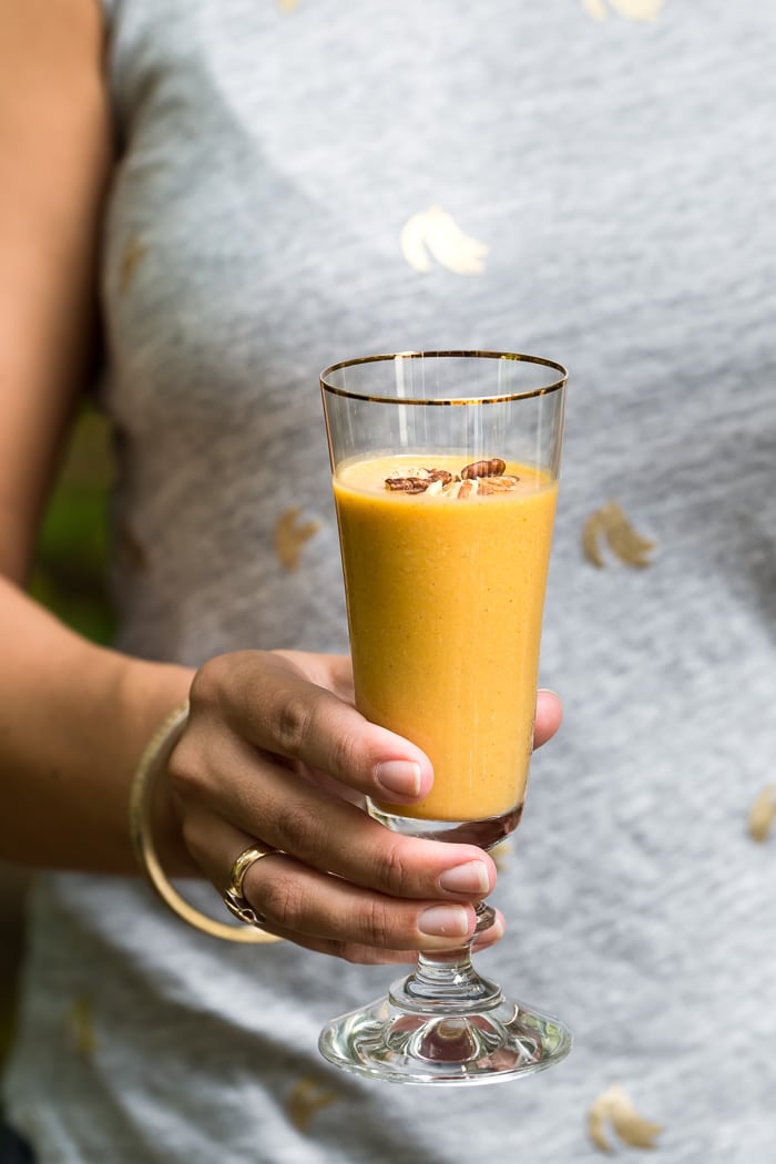 A woman is holding a glass of pumpkin protein smoothie in her hand