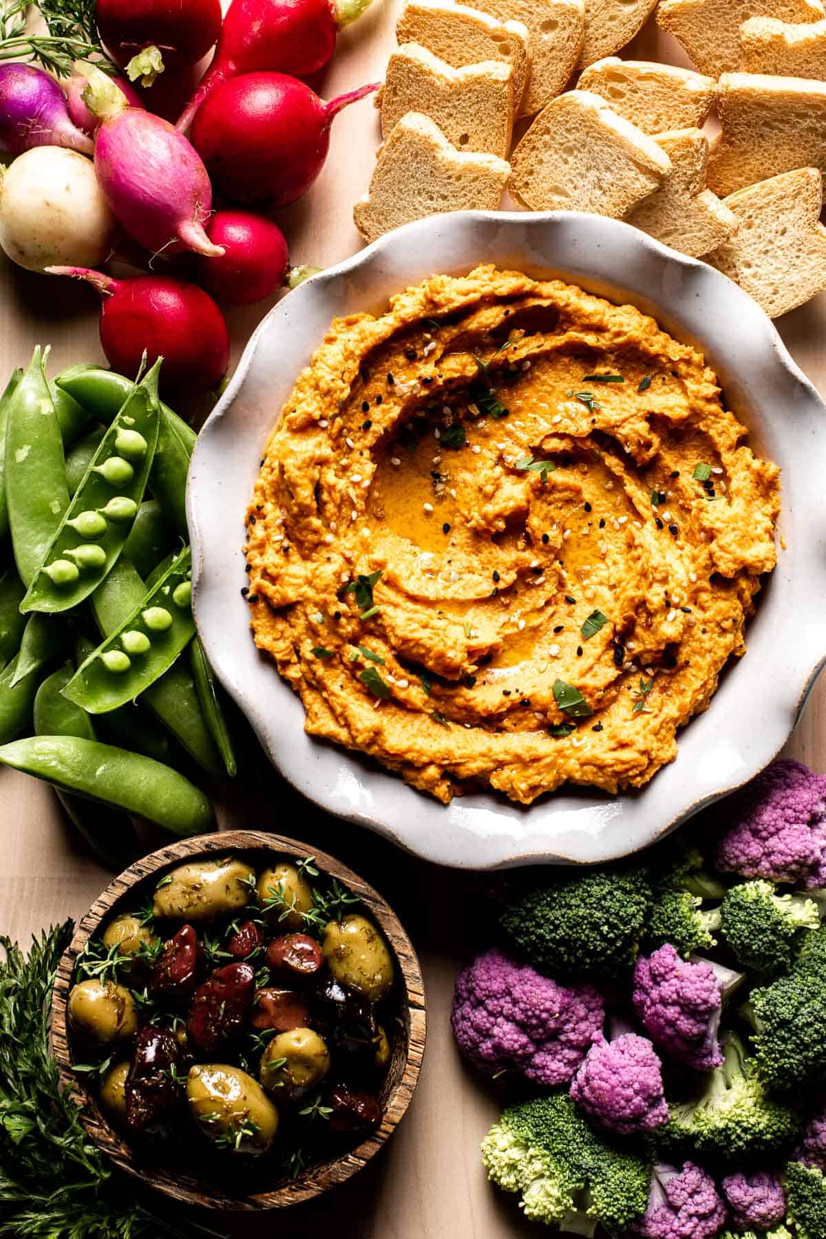 Roasted Carrot Hummus in a bowl with vegetables and olives around it