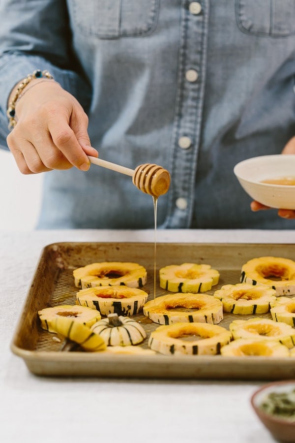 a woman is drizzling delicata squash with honey