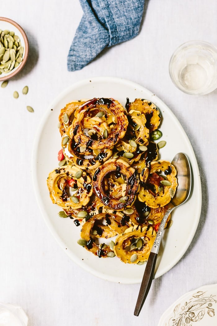 Recipe for Roasted Delicata Squash garnished with pumpkin seeds with a spoon on the side