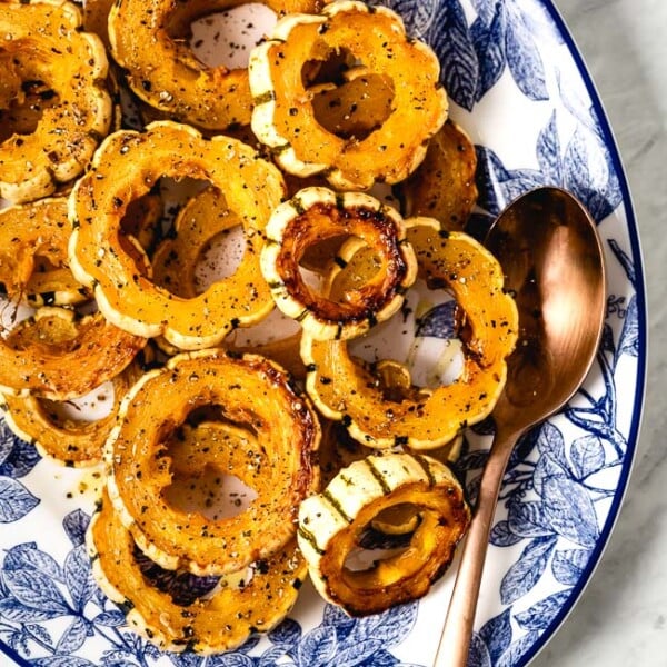 Roasted Delicata squash rings placed in an oval plated with a spoon on the side.