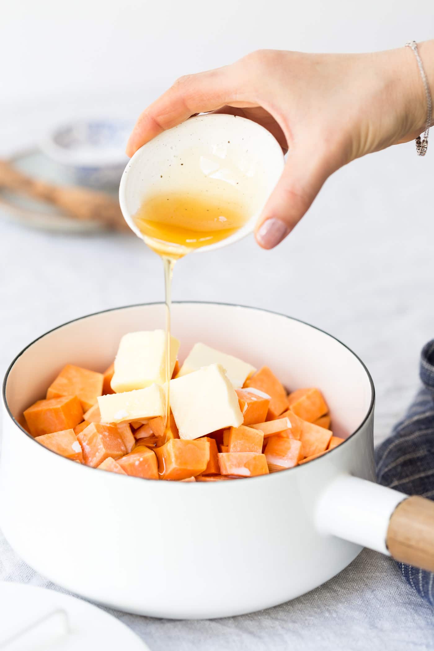 Learn how to make mashed sweet potato recipe - A woman is pouring maple syrup into butter and sweet potato mixture.