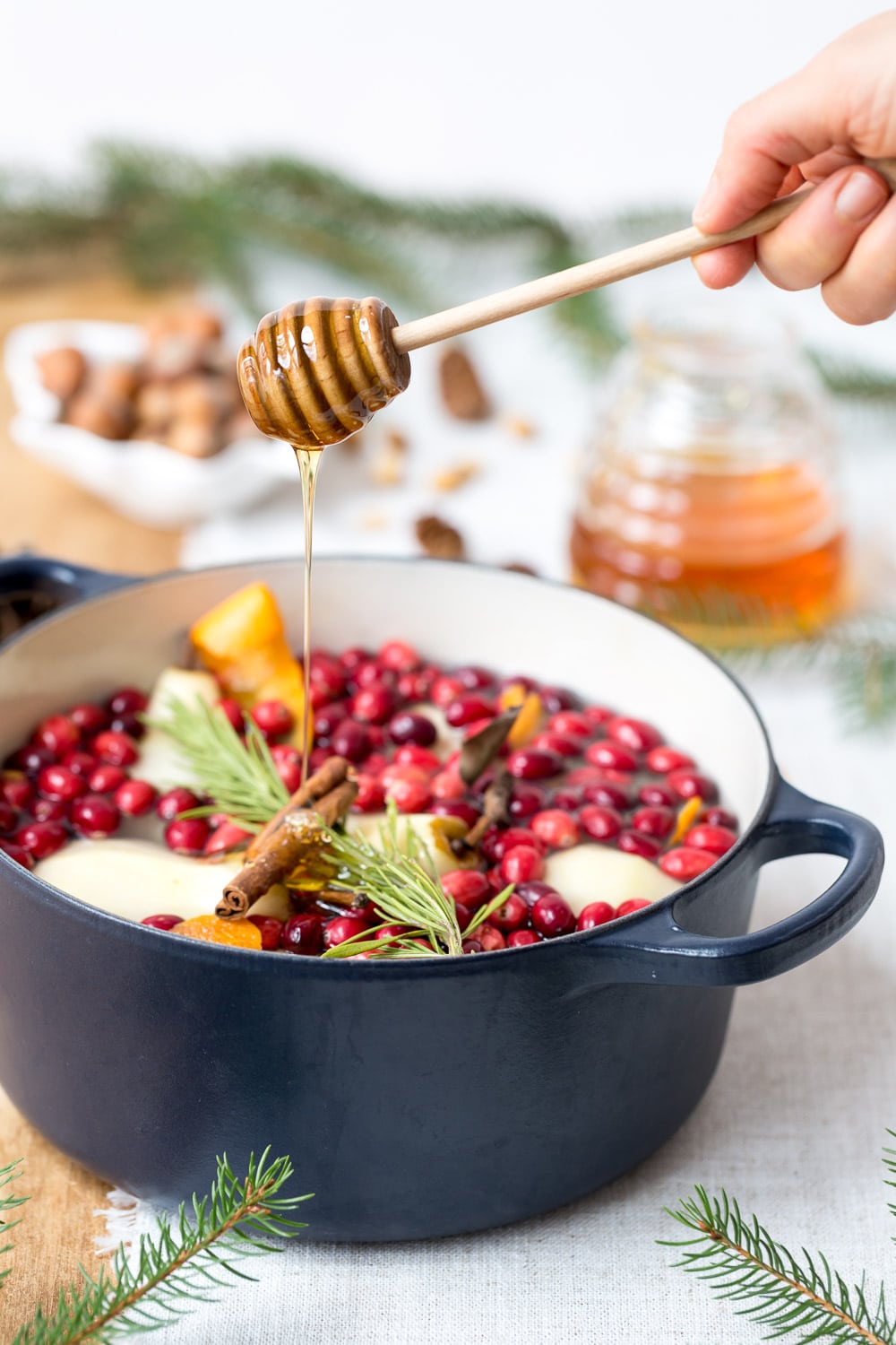 Honey is being drizzled in a big pot of cranberry poached pears