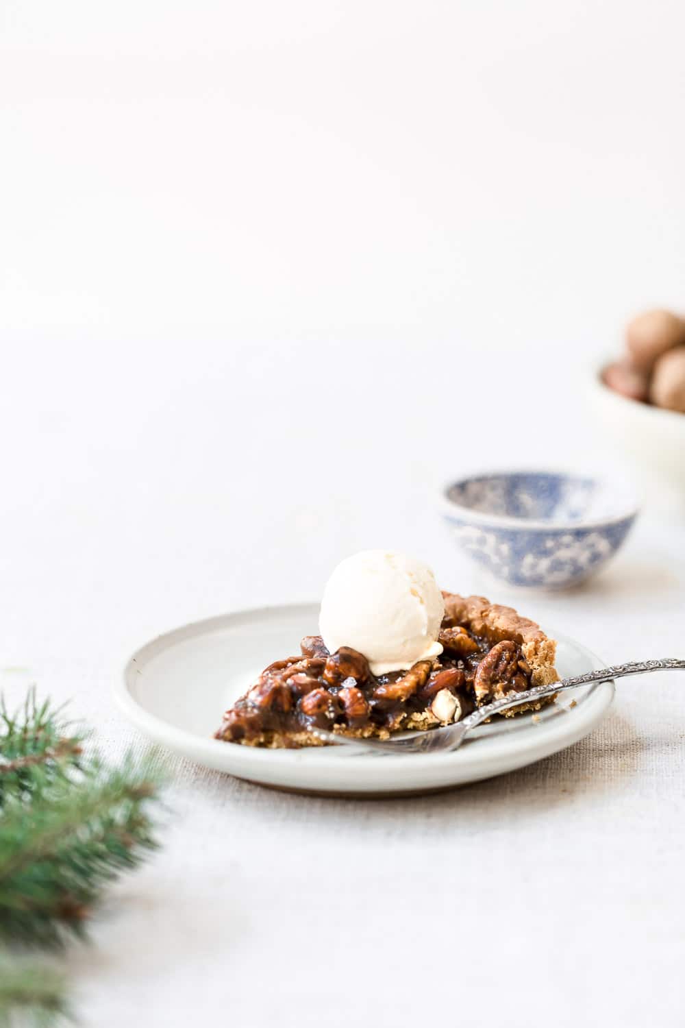 A slice of caramel nut tart topped off with a scoop of ice cream and photographed from the front view.