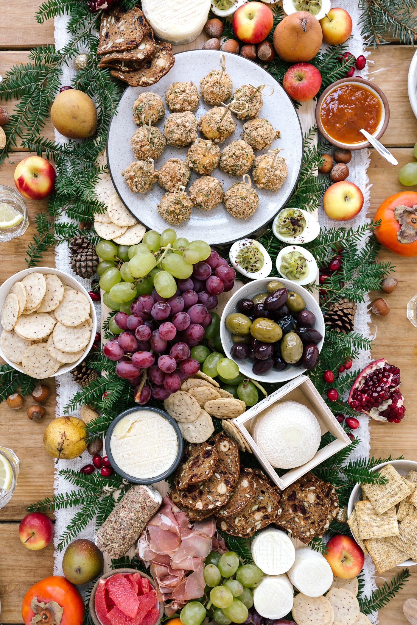 A big table set up cheese, fruit, baked goat cheese balls, and other edible goodies photographed from the top view.