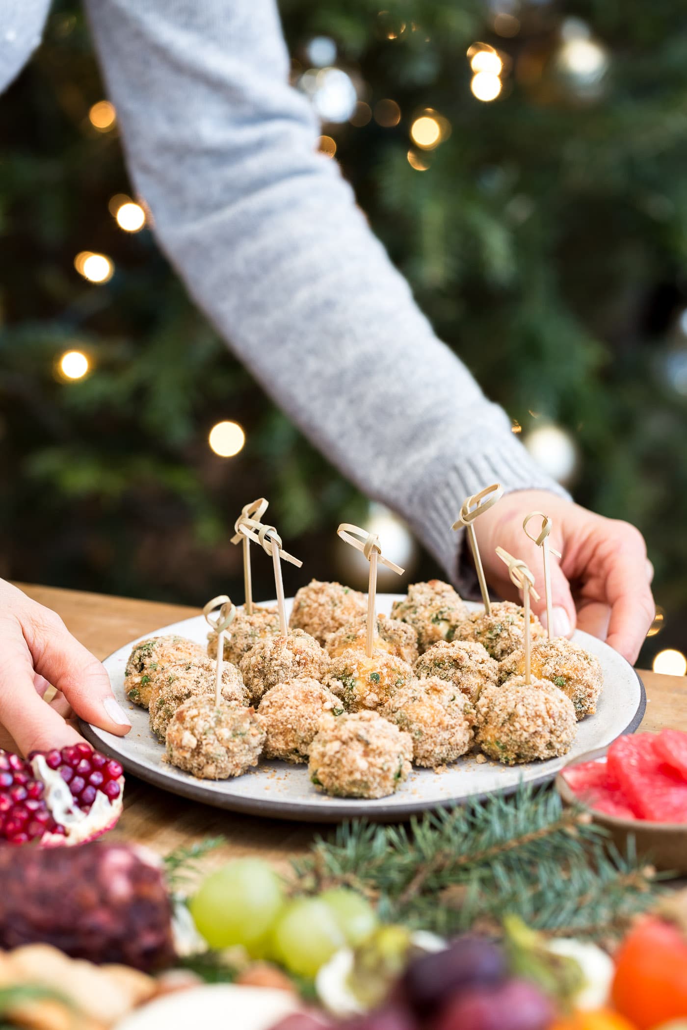 A woman is photographed as she is placing a plate of baked goat cheese balls on a plate.