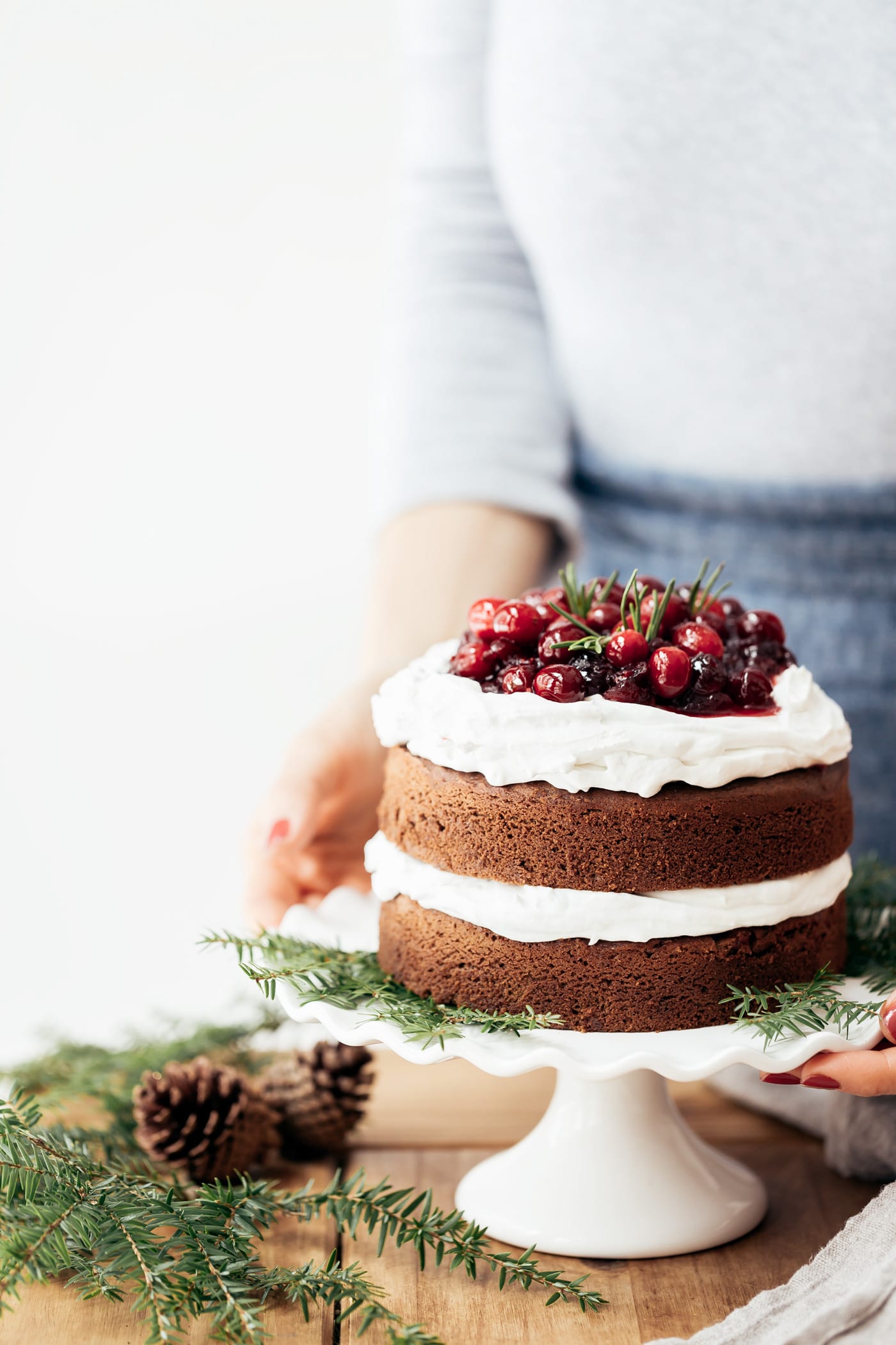 A woman is placing a gluten free gingerbread cake topped off with cranberries on the table.