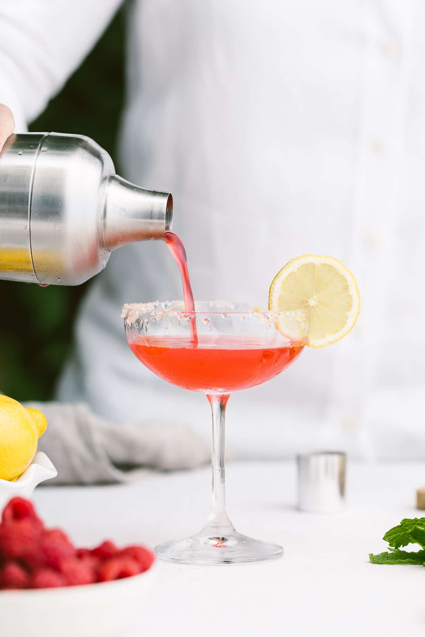 A woman is photographed as she is pouring raspberry lemon drop martini into a cocktail glass from the front view.