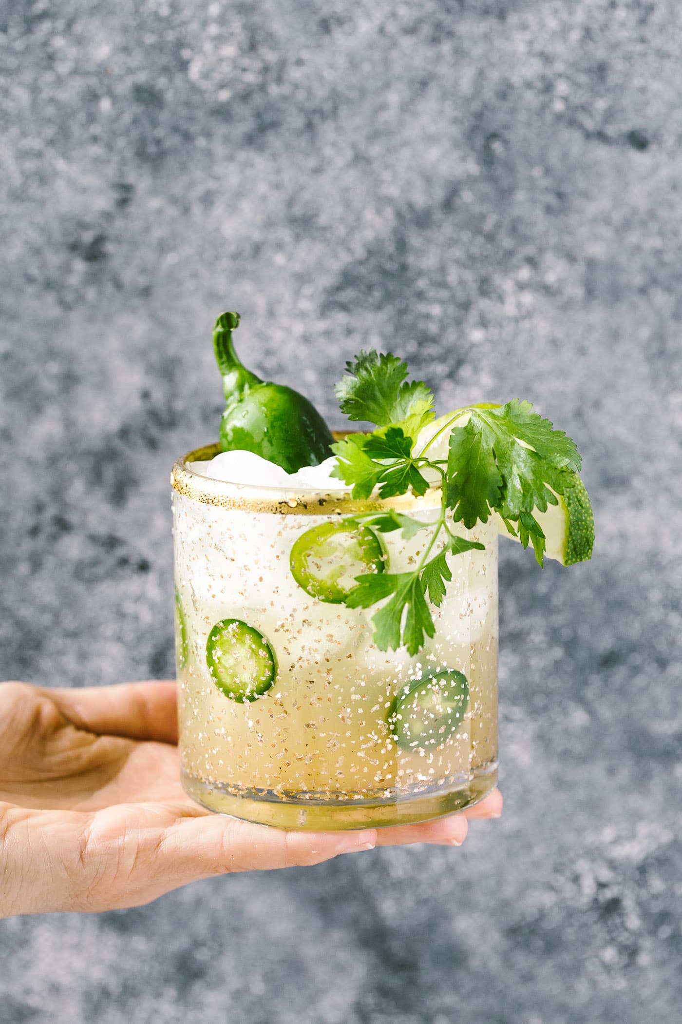 A woman is photographed from the front view as she is holding a spicy jalapeno margaritas in her hand.