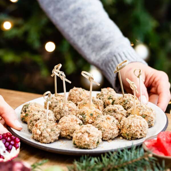 Baked goat cheese balls served on a platter by a woman in a festive background.