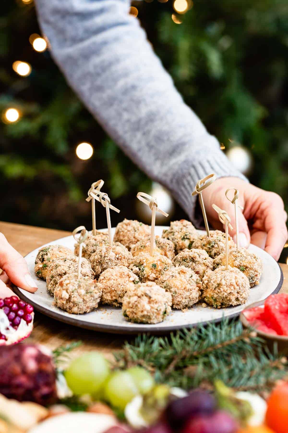 Baked goat cheese balls served on a platter by a woman in a festive background.