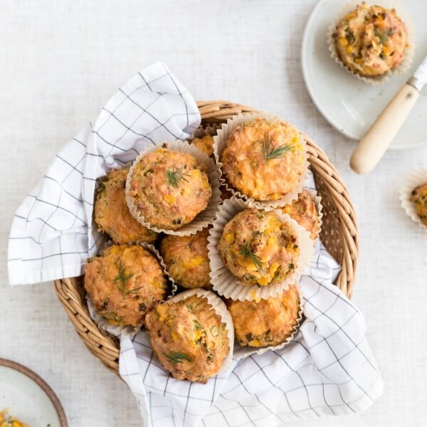 A basket full of freshly baked savory corn muffins along with a few half eaten ones are photographed from the top view.